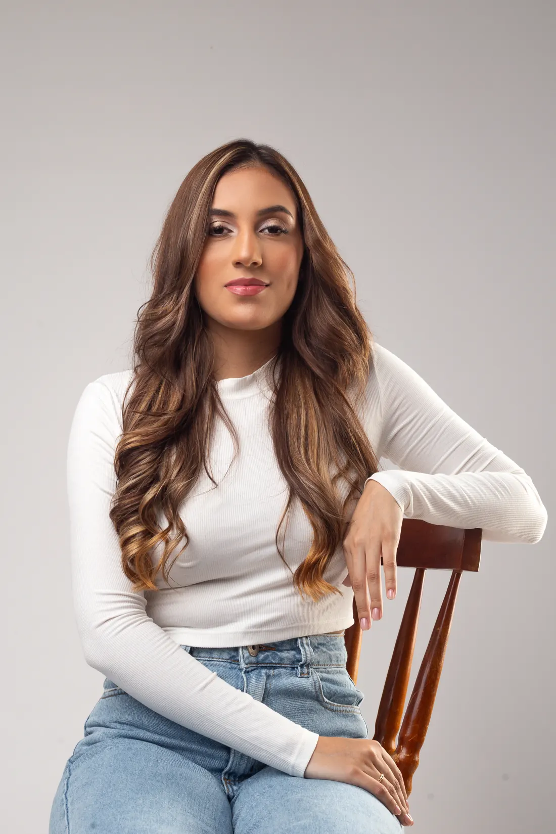 Nicoly sentada em uma cadeira de madeira, sorrindo